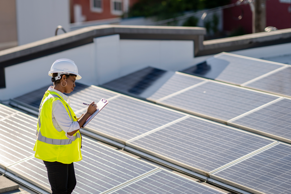 Femme munie d’un casque et d’un gilet réflecteur inspectant un toit couvert de panneaux solaires