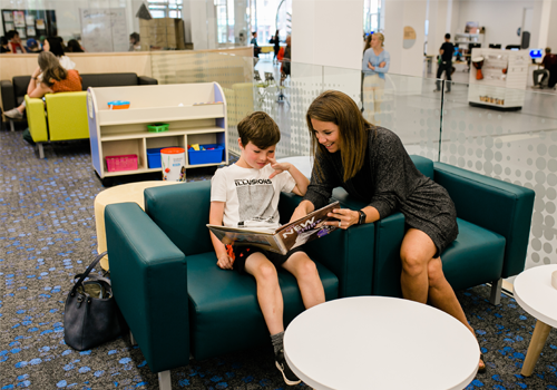 Un parent et son enfant assis ensemble sur un canapé, en train de lire un livre.