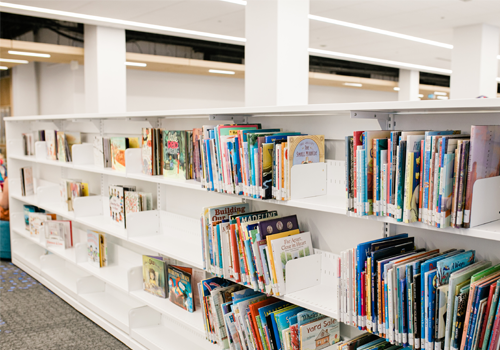 Une section pour enfants bien organisée dans une bibliothèque avec des étagères blanches basses remplies de livres colorés.