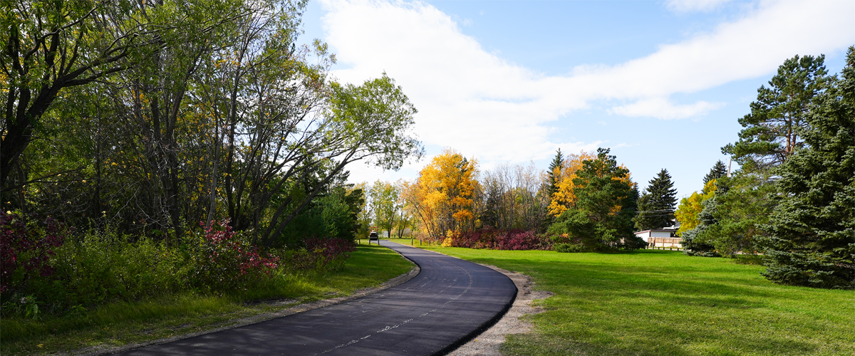 Un sentier asphalté longeant une pelouse bien entretenue avec des arbres en arrière-plan. 